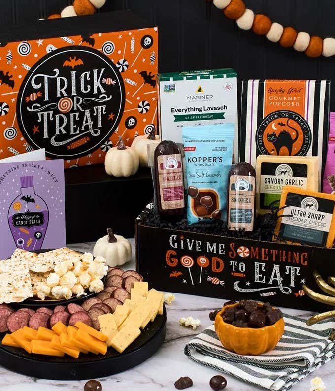 A Halloween-themed gift box featuring a variety of snacks, including cheddar cheese, summer sausage, crackers, gourmet popcorn, black and white cookies, gummy bears, and chocolate-covered treats, with a 