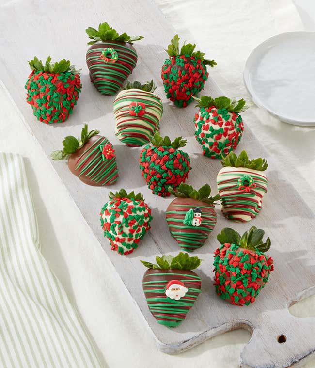 A festive assortment of chocolate-covered strawberries decorated with red and green sprinkles, holiday-themed designs, and colorful drizzles, arranged on a white plate.