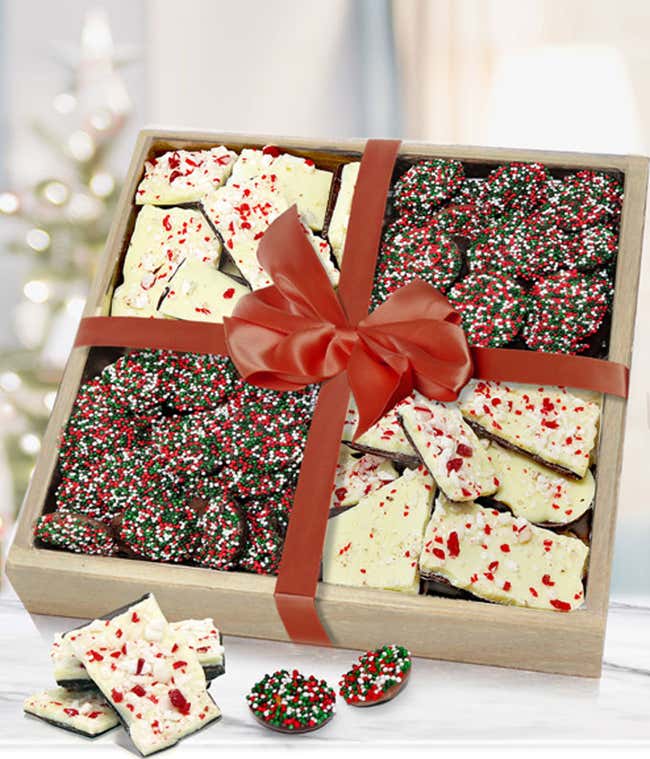 Festive gift box filled with holiday treats, including peppermint bark and chocolate-covered pretzels decorated with red, green, and white sprinkles. The box is tied with a red ribbon and bow, creating a cheerful holiday presentation.
