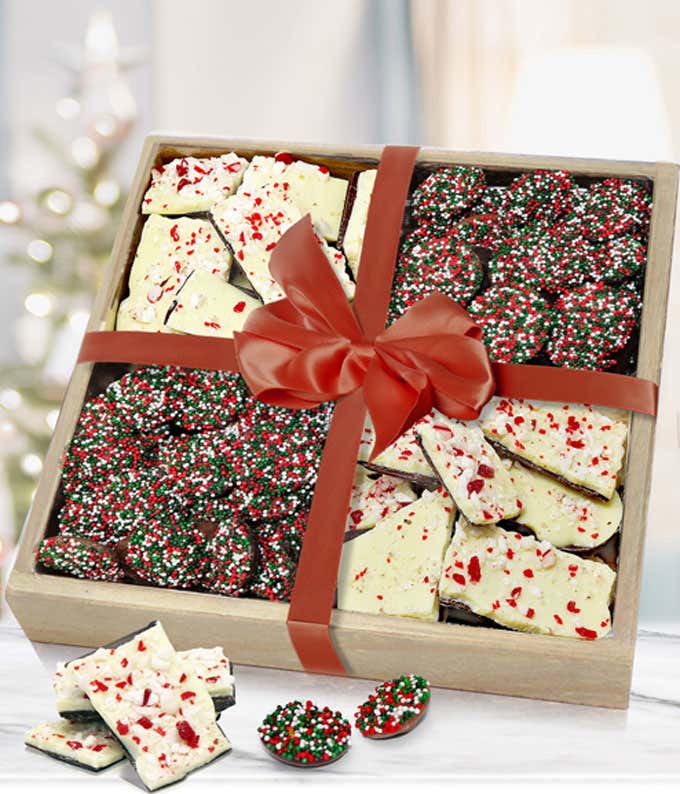 Festive gift box filled with holiday treats, including peppermint bark and chocolate-covered pretzels decorated with red, green, and white sprinkles. The box is tied with a red ribbon and bow, creating a cheerful holiday presentation.