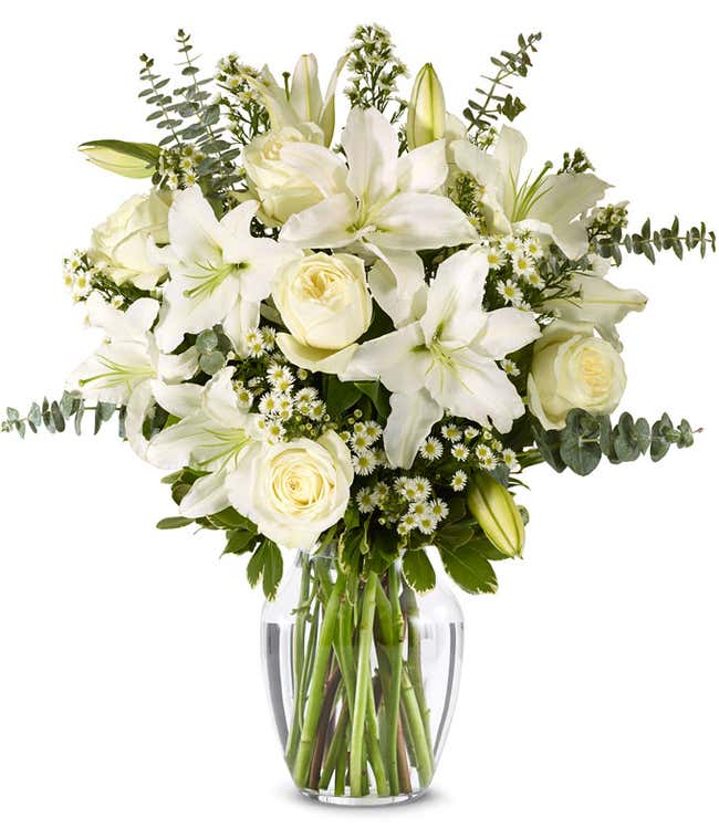 An elegant floral arrangement featuring white roses, white lilies, white asters, and eucalyptus, optionally displayed in a glass vase.