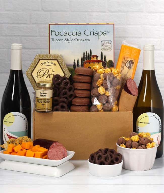 A gift set featuring two bottles of Hill &amp; Harbor wine - white and red, focaccia crisps, 2 cheeses, mustard, summer sausage, caramel popcorn, chocolate pretzels, and 6 chocolate-covered Oreos for a sweet and savory gourmet experience.