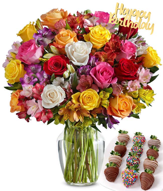 Colorful birthday flower bouquet with mixed roses and alstroemeria in a clear glass vase, topped with a gold &ldquo;Happy Birthday&rdquo; pick, paired with an assortment of chocolate-covered strawberries decorated with sprinkles and drizzles.
