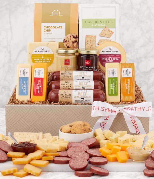 Sympathy gift basket filled with assorted Hickory Farms cheeses, summer sausages, mustard, crackers, and chocolate chip cookies, displayed with a cutting board and garnished with a sympathy ribbon.