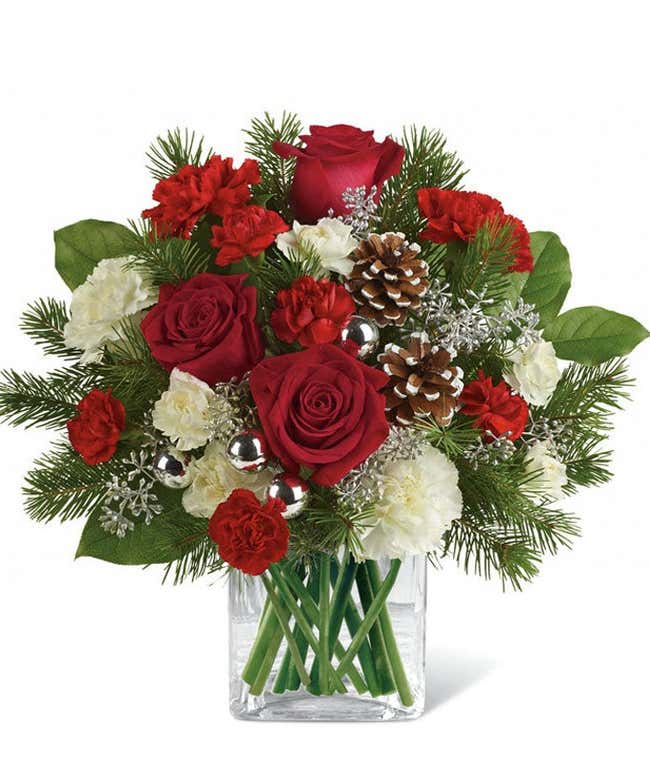 A festive arrangement with red roses (deluxe &amp; premium only), red carnations, white carnations, red mini-carnations, white mini-carnations, seasonal greens, silver ornaments, and pine cones.