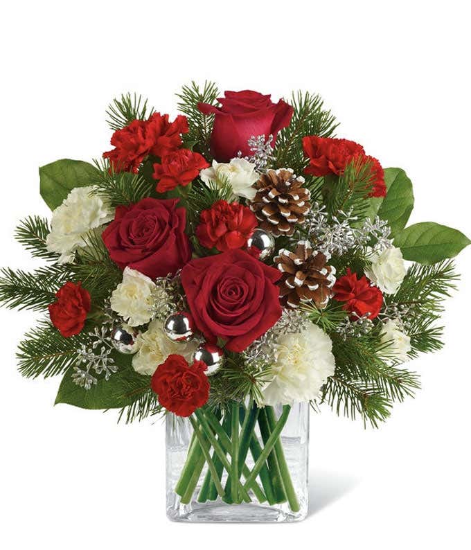 A festive arrangement with red roses (deluxe & premium only), red carnations, white carnations, red mini-carnations, white mini-carnations, seasonal greens, silver ornaments, and pine cones.