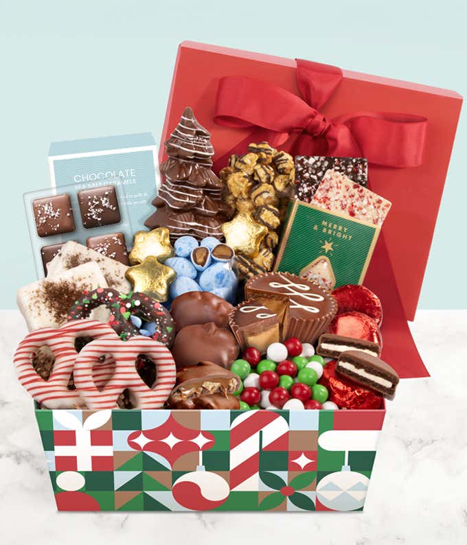 Festive gift box filled with assorted holiday treats, including chocolate-covered pretzels, popcorn, chocolate bark, cookies, colorful candy-coated chocolates, and holiday-themed chocolate bars, decorated with a red ribbon.