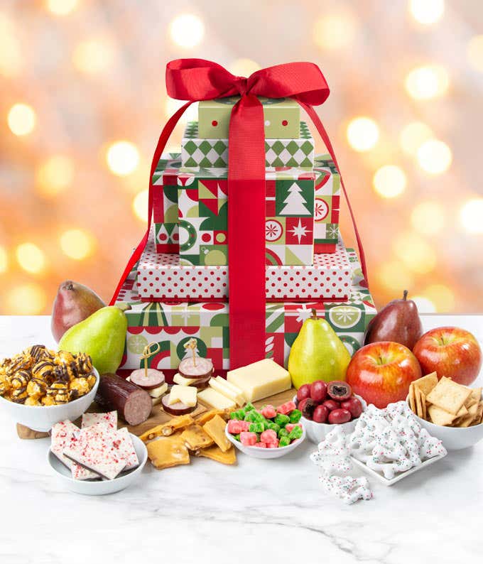 A festive holiday-themed gift tower adorned with a large red bow. Inside the tower are fresh pears, apples, blocks of cheese, crackers, peppermint bark, popcorn, and assorted holiday treats. 