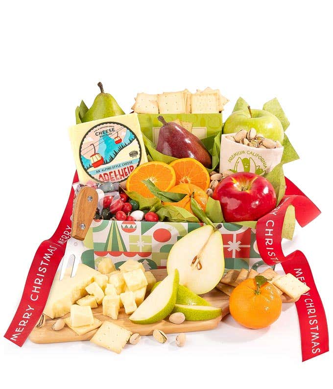 A holiday gift box filled with fresh apples, pears, oranges, crackers, cheese, pistachios, and festive holiday candies, all arranged with green tissue paper for a festive presentation. 