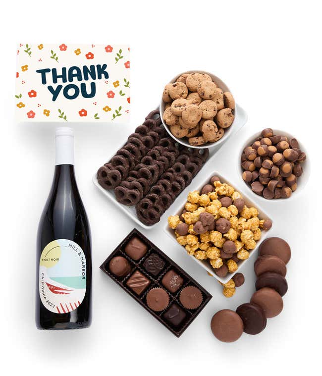 A gift box overflowing with treats including an assortment of chocolate-covered items like oreoes, almonds, graham crackers and pretzels along with red velvet cookies, hazelnut wafers, an 8 piece box of chocolates and a bottle of red wine.