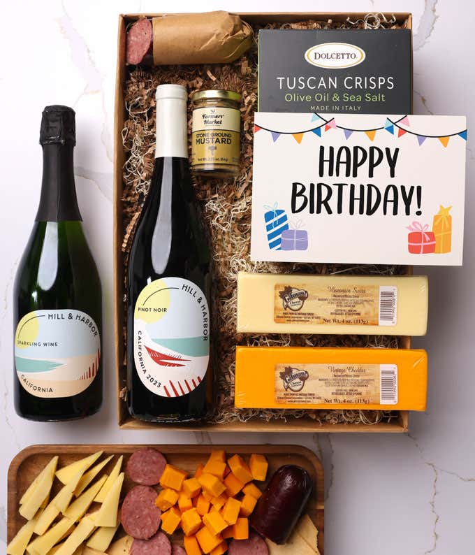 A gift box with two bottles of California wine (Pinot Noir and Sparkling Wine), two types of cheese, crackers, stone-ground mustard, a summer sausage, and a cheerful birthday card. 