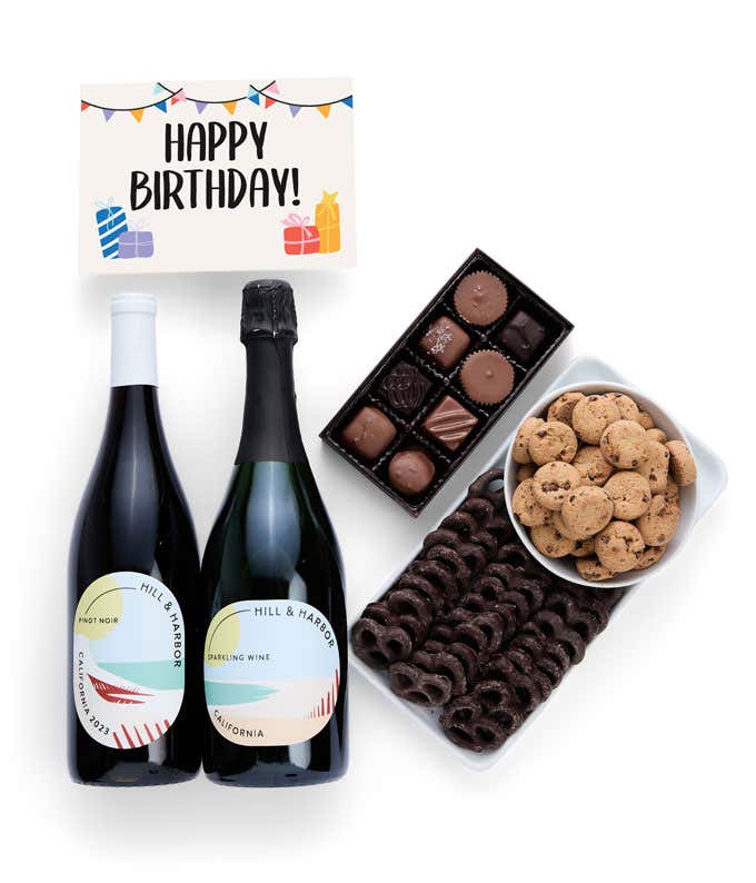 A gift box with chocolate pretzels, chocolate graham crackers, red velvet cookies, hazelnut wafer rolls, an 8 piece box of chocolates, 2 bottles of wine and a Birthday message card.