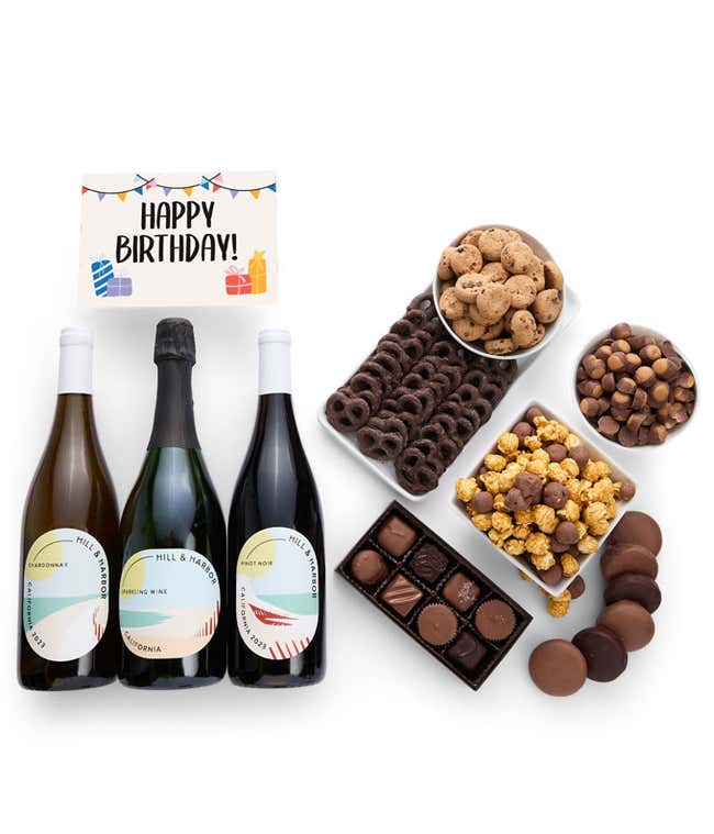 A gift box overflowing with treats including an assortment of chocolate-covered items like oreoes, almonds graham crackers and pretzels along with red velvet cookies, hazelnut wafers, an 8 piece box of chocolates, 3 bottles of wine and a Birthday card.