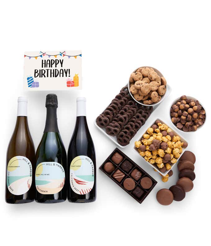 A gift box overflowing with treats including an assortment of chocolate-covered items like oreoes, almonds graham crackers and pretzels along with red velvet cookies, hazelnut wafers, an 8 piece box of chocolates, 3 bottles of wine and a Birthday card.