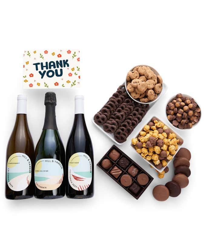 A gift box overflowing with treats including an assortment of chocolate-covered items like oreoes, almonds graham crackers and pretzels along with red velvet cookies, hazelnut wafers, an 8 piece box of chocolates, 3 bottles of wine and a Thank You card.