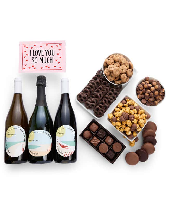 A gift box overflowing with treats including an assortment of chocolate-covered items like oreoes, almonds graham crackers and pretzels along with red velvet cookies, hazelnut wafers, an 8 piece box of chocolates, 3 bottles of wine and an I Love You card.